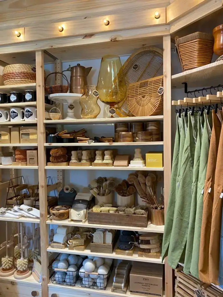 Shelves displaying eco-friendly home goods, brushes, glassware, baskets, and linen aprons.