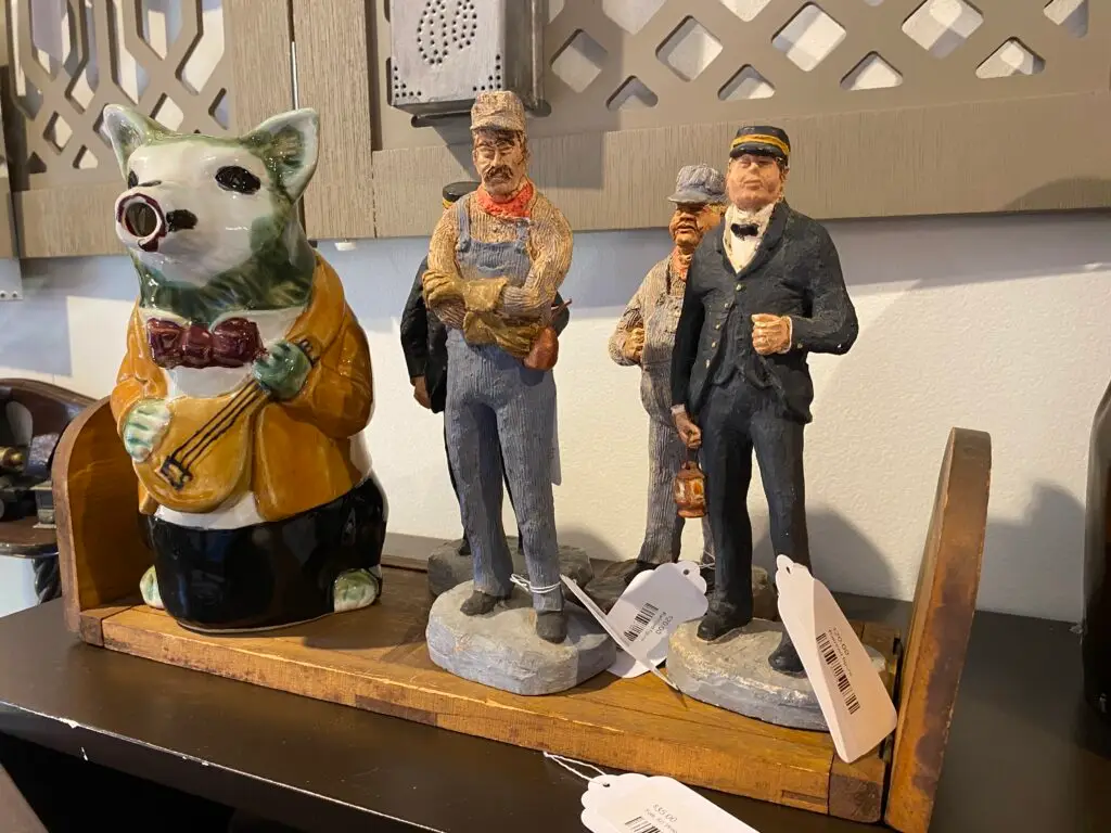 Hand-carved vintage figurines and ceramic animal sculpture displayed on a wooden shelf inside Starshine Designs and Eclectic Finds.